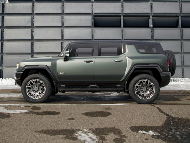 Side view of the 2024 GMC Hummer EV SUV in green parked in front of a modern metal-paneled building