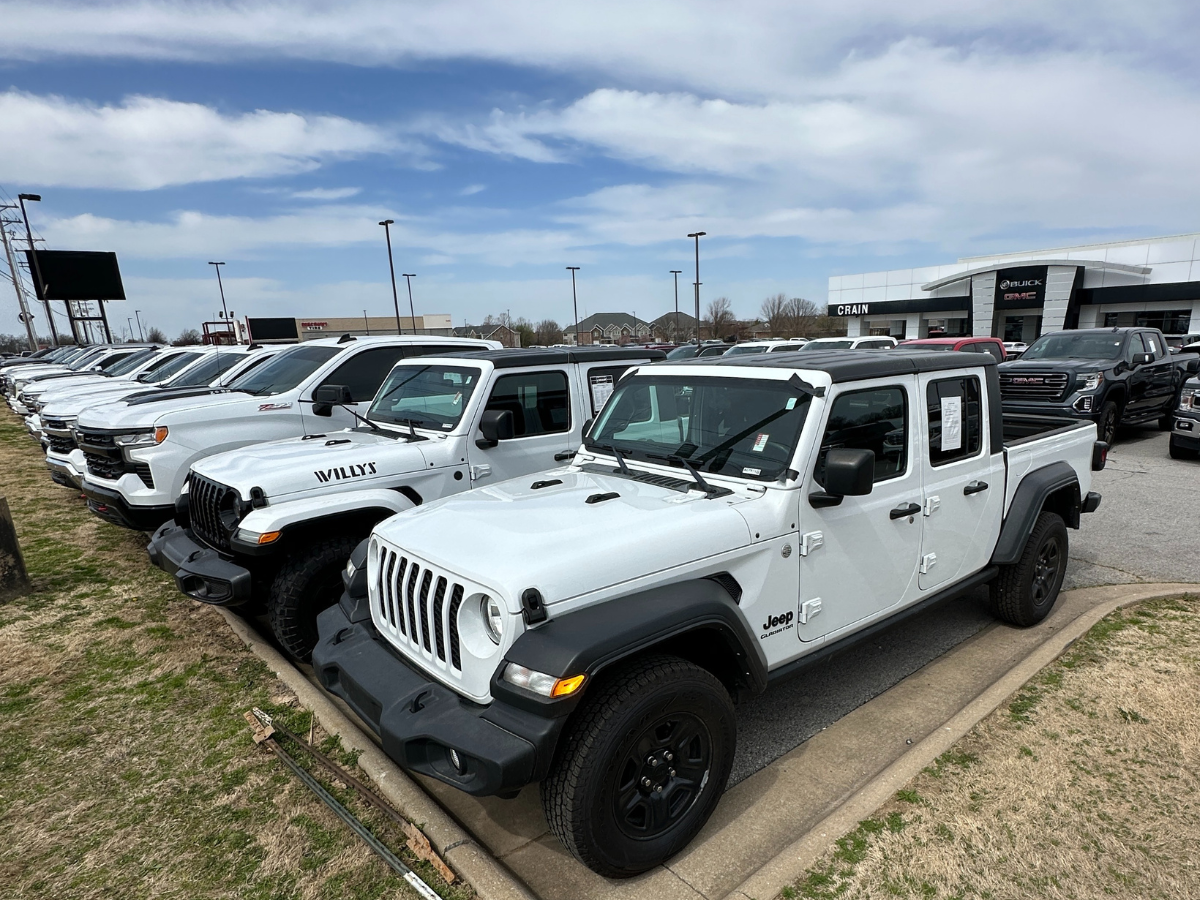 Lineup of used white pickup trucks and SUVs, including a Jeep Gladiator Willys and Chevy Silverado, at Crain Buick GMC in Springdale, Arkansas